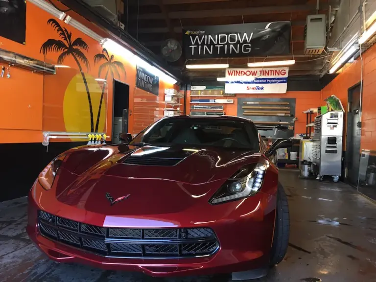 Red Corvette Stingray inside the shop under the palm-tree mural and Window Tinting sign