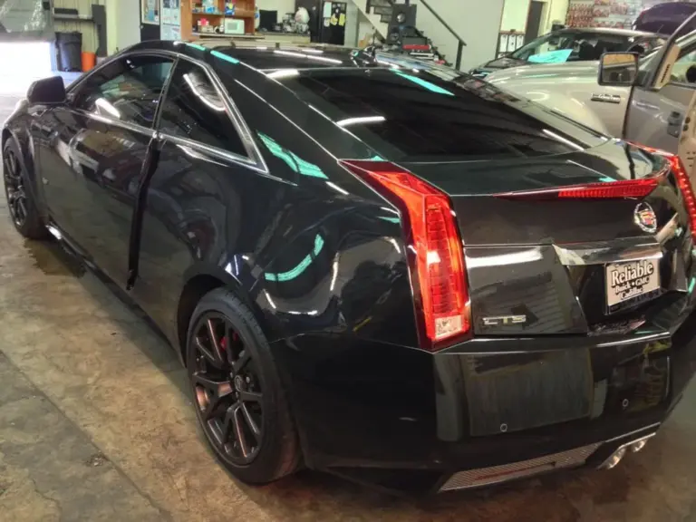Black Cadillac CTS coupe with tinted windows, door open, in the shop