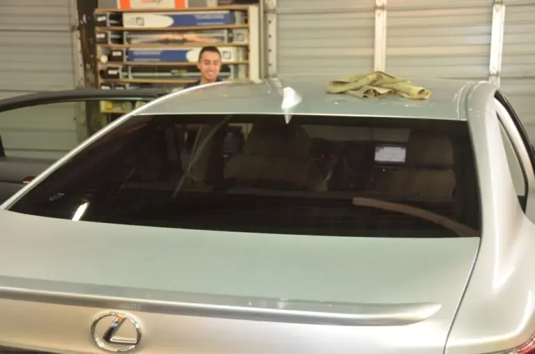 Silver Lexus with a freshly tinted rear window, installer behind it