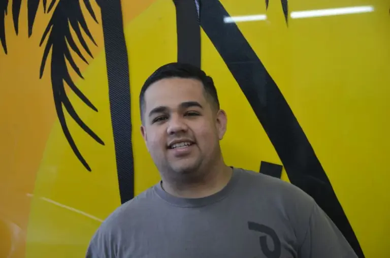 Smiling Shades of California team member by the palm-tree mural
